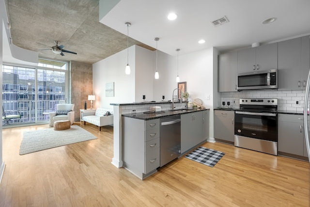 kitchen with pendant lighting, sink, dark stone countertops, kitchen peninsula, and stainless steel appliances