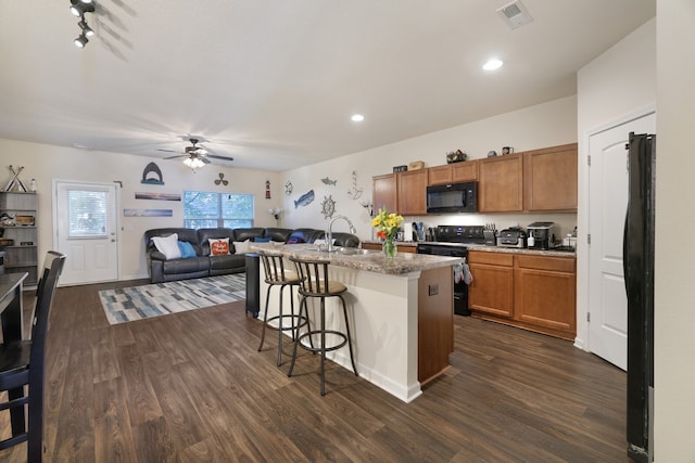 kitchen featuring black appliances, sink, dark wood-type flooring, a breakfast bar, and a kitchen island with sink