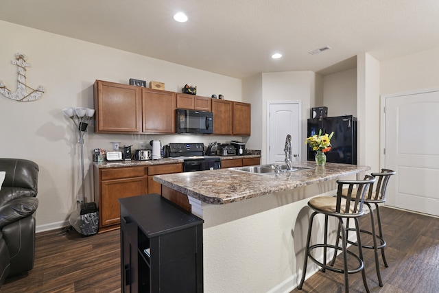 kitchen featuring a center island with sink, black appliances, and dark hardwood / wood-style flooring