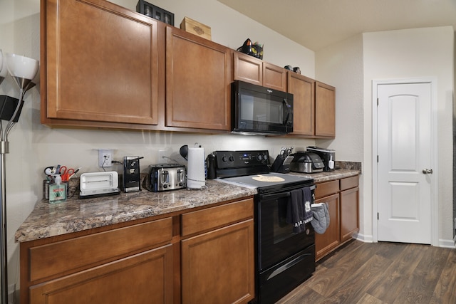 kitchen with dark stone countertops, black appliances, and dark hardwood / wood-style flooring