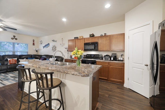 kitchen featuring a center island with sink, a breakfast bar area, dark hardwood / wood-style flooring, black appliances, and sink