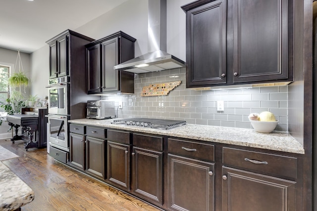 kitchen with wall chimney exhaust hood, hardwood / wood-style flooring, stainless steel appliances, and dark brown cabinets