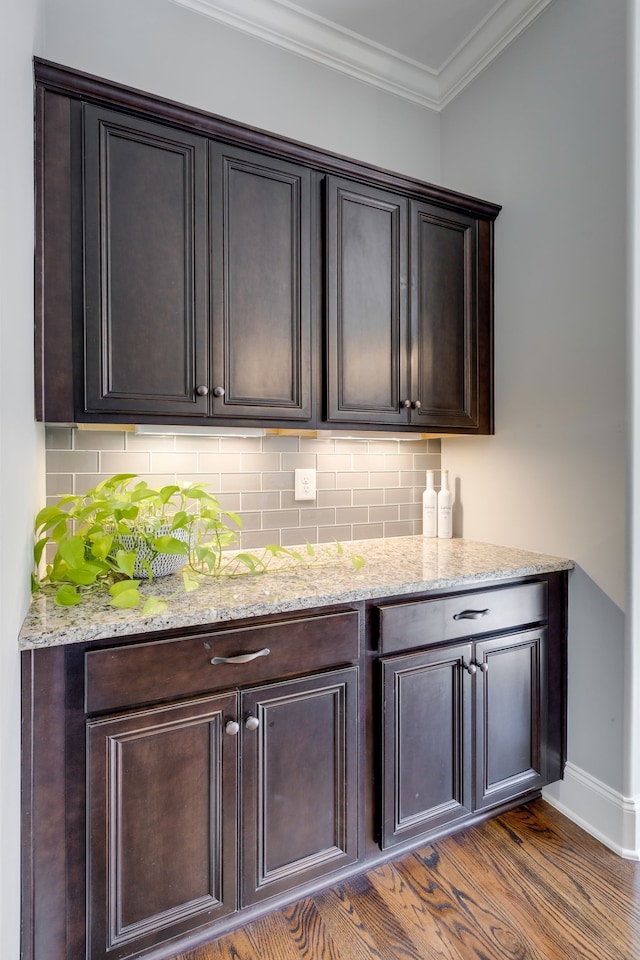 bar with crown molding, dark brown cabinetry, tasteful backsplash, and dark hardwood / wood-style flooring