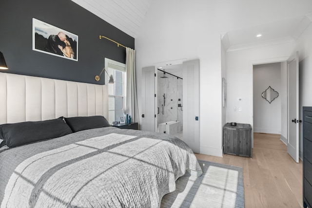 bedroom featuring light hardwood / wood-style flooring, ensuite bath, and high vaulted ceiling