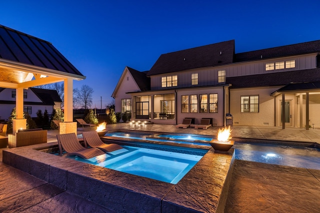 pool at dusk featuring an in ground hot tub, an outdoor fire pit, and a patio