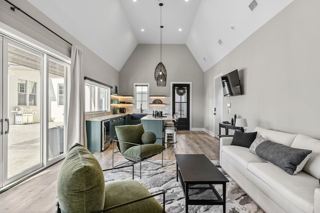 living room featuring light hardwood / wood-style floors, high vaulted ceiling, bar area, and beverage cooler