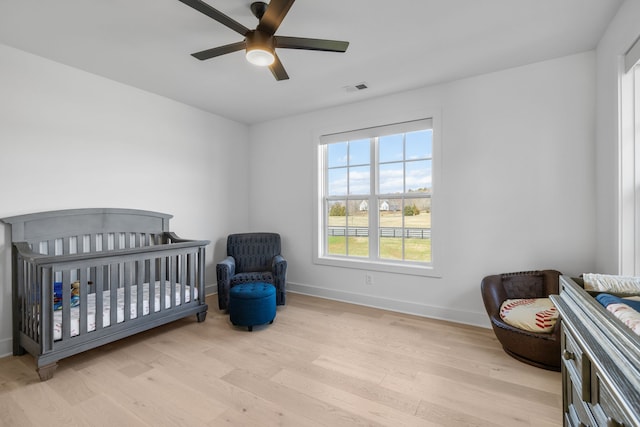 bedroom featuring ceiling fan, light hardwood / wood-style flooring, and a crib