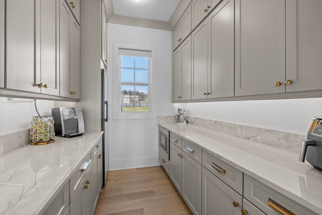 kitchen with light hardwood / wood-style flooring, light stone counters, gray cabinetry, and stainless steel microwave