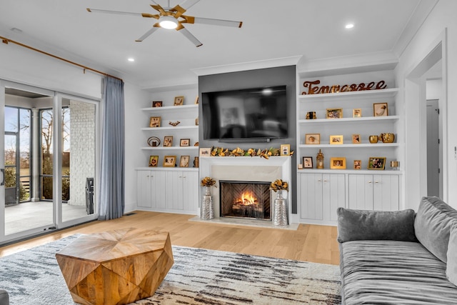 living room with crown molding, built in shelves, light hardwood / wood-style floors, and ceiling fan