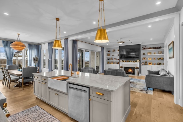 kitchen featuring light stone counters, light wood-type flooring, a center island with sink, and hanging light fixtures