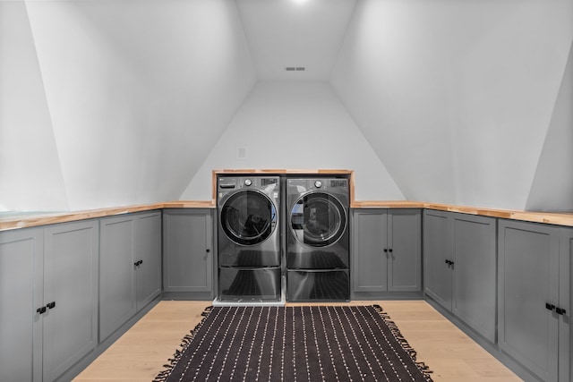 clothes washing area featuring independent washer and dryer, cabinets, and light hardwood / wood-style flooring