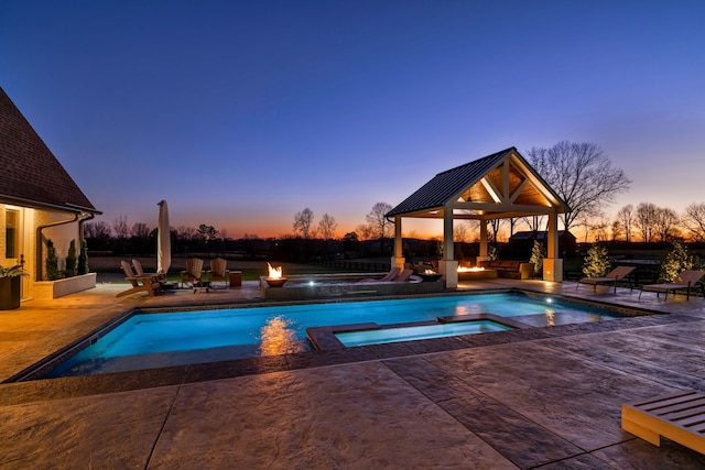 pool at dusk with a gazebo, an in ground hot tub, and a patio area