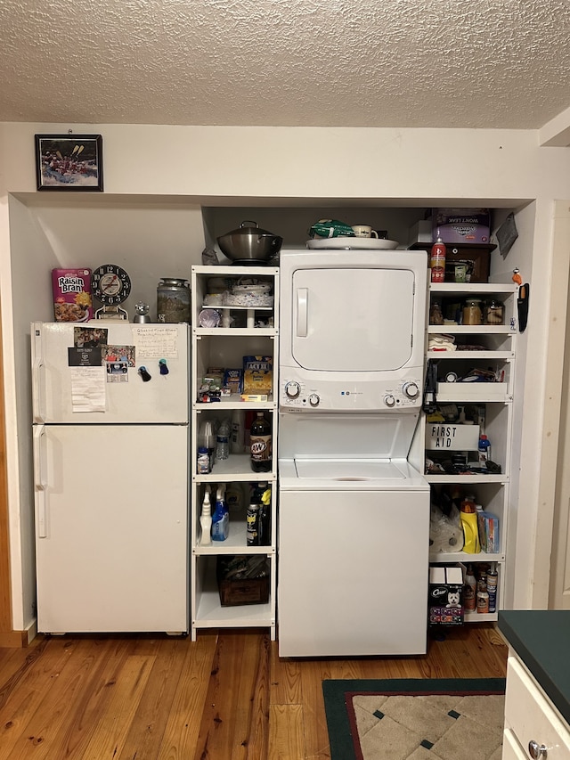 laundry area featuring stacked washing maching and dryer, hardwood / wood-style flooring, and a textured ceiling