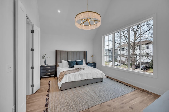 bedroom featuring a notable chandelier, light hardwood / wood-style flooring, and vaulted ceiling