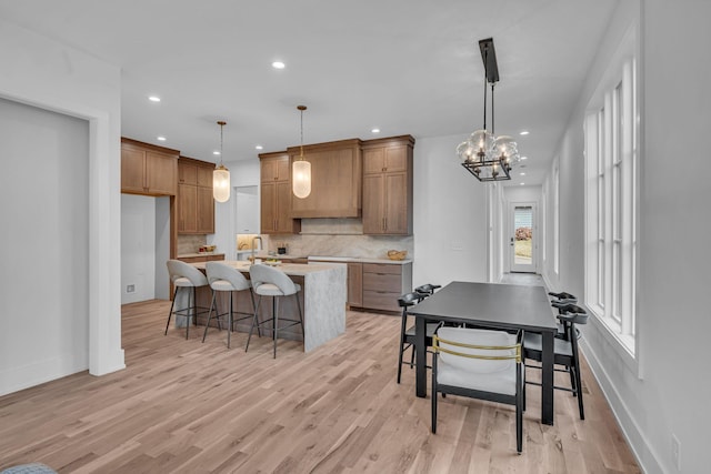 kitchen featuring decorative light fixtures, backsplash, an island with sink, light hardwood / wood-style floors, and wall chimney range hood