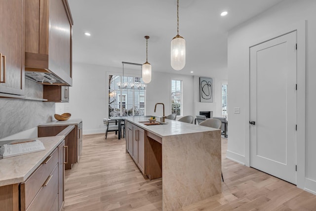 kitchen featuring sink, decorative light fixtures, a kitchen island with sink, and light wood-type flooring