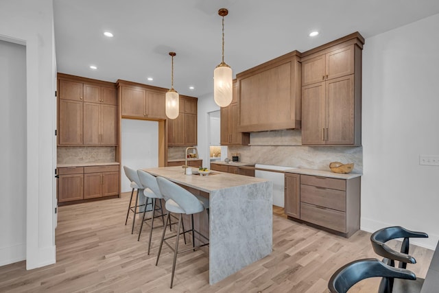 kitchen featuring sink, tasteful backsplash, hanging light fixtures, a kitchen island with sink, and light hardwood / wood-style floors