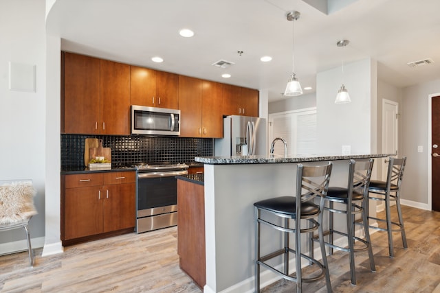 kitchen with an island with sink, stainless steel appliances, and light wood-type flooring