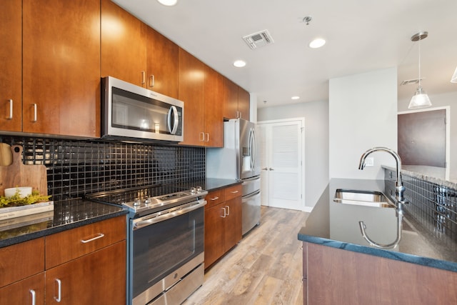 kitchen featuring appliances with stainless steel finishes, sink, backsplash, light hardwood / wood-style floors, and pendant lighting