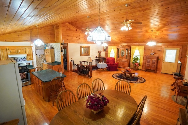 dining space with ceiling fan with notable chandelier, wooden ceiling, wooden walls, high vaulted ceiling, and light hardwood / wood-style flooring