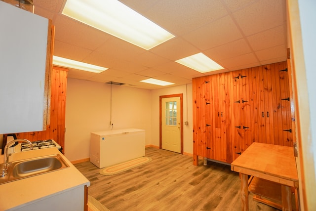 interior space featuring wooden walls, hardwood / wood-style floors, sink, a drop ceiling, and refrigerator