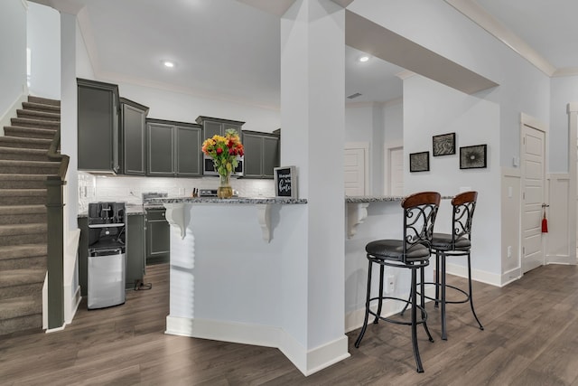 kitchen featuring a kitchen breakfast bar, light stone counters, ornamental molding, and dark wood-type flooring