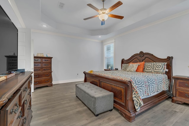 bedroom with wood-type flooring, a tray ceiling, ceiling fan, and ornamental molding