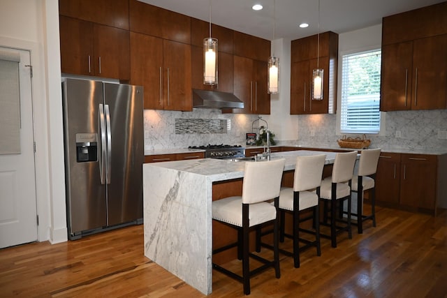 kitchen with an island with sink, stainless steel appliances, dark hardwood / wood-style floors, a kitchen breakfast bar, and hanging light fixtures