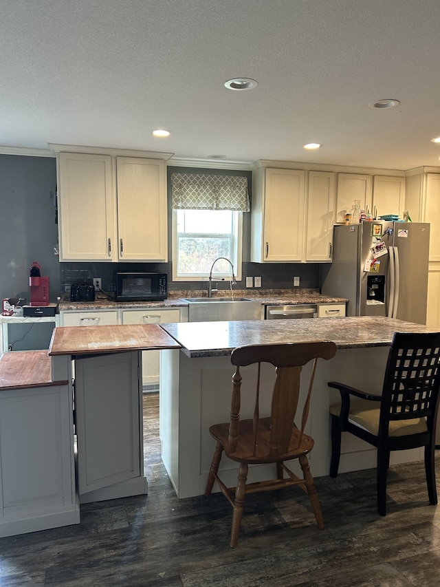 kitchen with dark hardwood / wood-style flooring, a kitchen bar, sink, stainless steel refrigerator with ice dispenser, and a center island