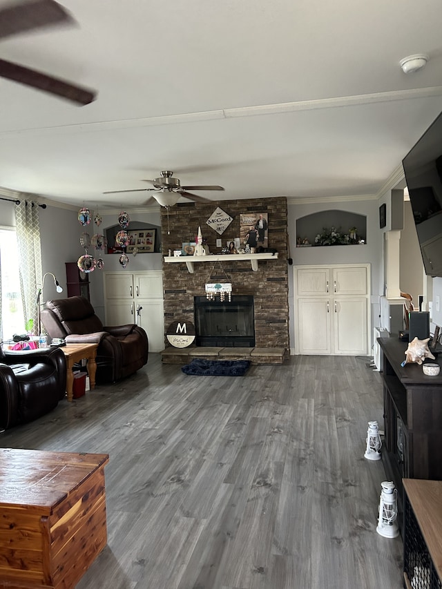 living room with ornamental molding, wood-type flooring, a large fireplace, and ceiling fan