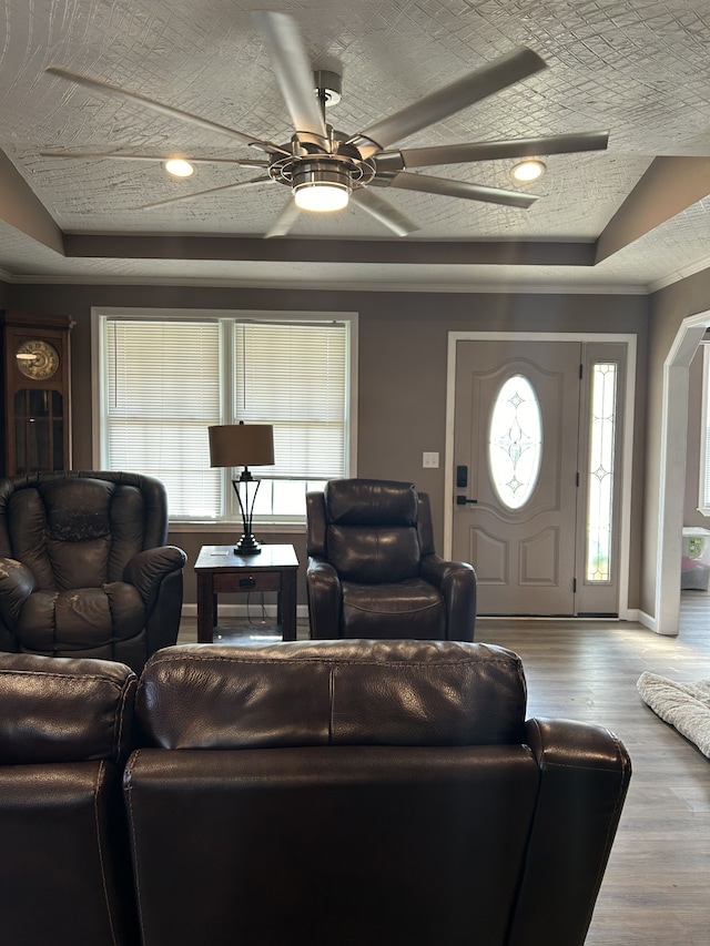 living room featuring a textured ceiling, wood-type flooring, a tray ceiling, and ceiling fan