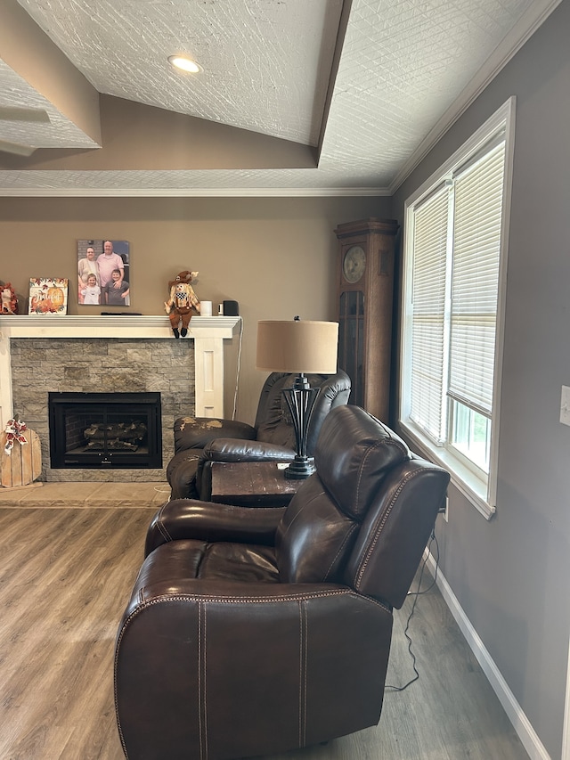 living room featuring hardwood / wood-style flooring, a textured ceiling, vaulted ceiling, and a stone fireplace