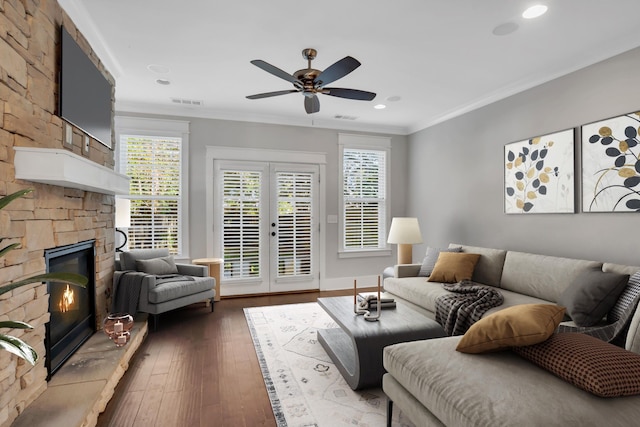 living room featuring ceiling fan, wood-type flooring, a fireplace, crown molding, and french doors