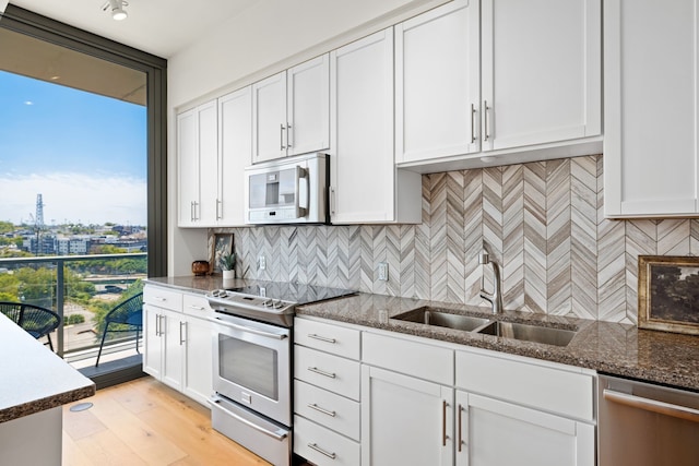 kitchen featuring sink, light hardwood / wood-style floors, stainless steel appliances, dark stone counters, and white cabinets