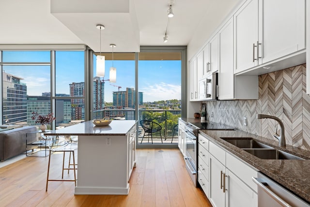 kitchen featuring appliances with stainless steel finishes, white cabinetry, light hardwood / wood-style flooring, dark stone countertops, and pendant lighting