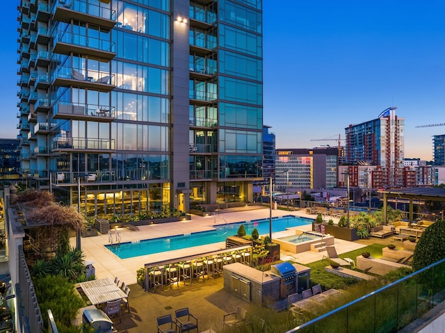 pool at dusk with a hot tub and a patio area