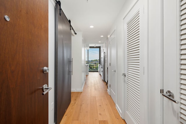 corridor with a barn door and light hardwood / wood-style floors