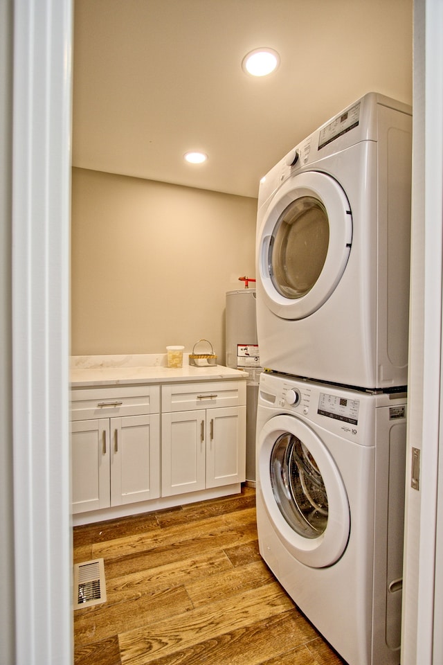 clothes washing area featuring stacked washer / drying machine, cabinets, and light hardwood / wood-style floors