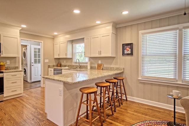 kitchen featuring kitchen peninsula, white cabinets, stacked washer / drying machine, light hardwood / wood-style floors, and sink