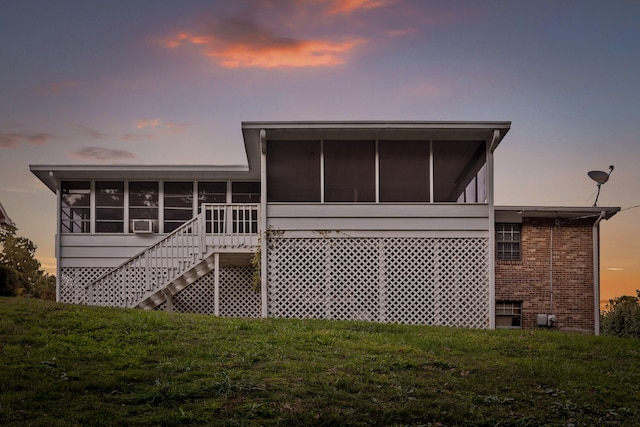 back house at dusk with a sunroom and a lawn