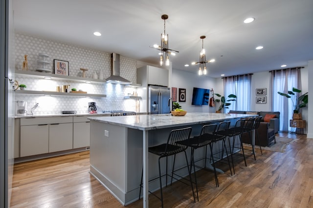 kitchen with wall chimney exhaust hood, a center island, light wood-type flooring, and stainless steel appliances