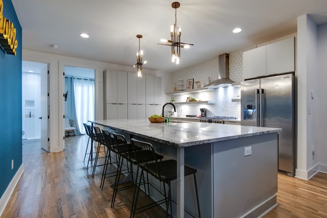 kitchen featuring high end refrigerator, wall chimney exhaust hood, light hardwood / wood-style flooring, decorative light fixtures, and white cabinets