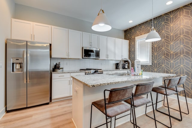 kitchen with decorative light fixtures, white cabinets, stainless steel appliances, and an island with sink