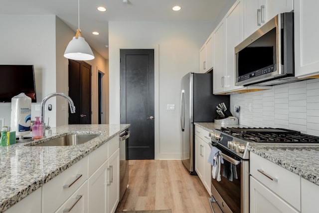 kitchen featuring sink, light wood-type flooring, white cabinetry, stainless steel appliances, and pendant lighting