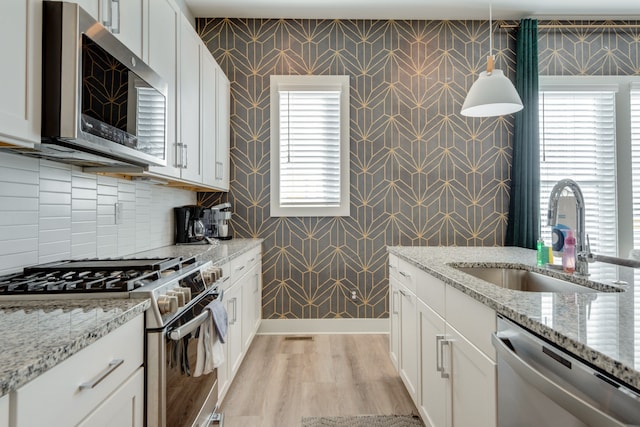 kitchen with appliances with stainless steel finishes, a healthy amount of sunlight, hanging light fixtures, and light hardwood / wood-style floors