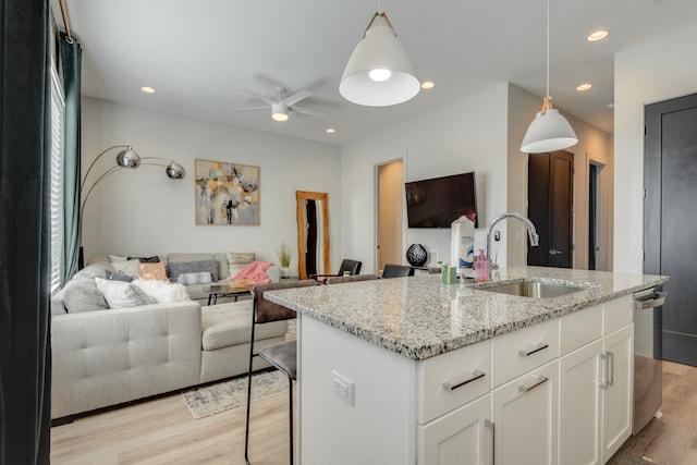 kitchen featuring sink, light wood-type flooring, a kitchen bar, pendant lighting, and white cabinets