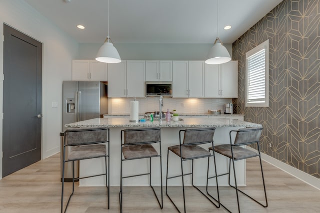 kitchen with white cabinets, a kitchen island with sink, light hardwood / wood-style flooring, decorative light fixtures, and light stone counters