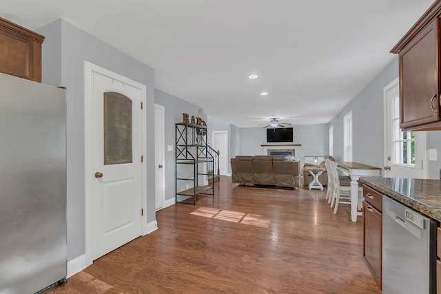 kitchen with appliances with stainless steel finishes, ceiling fan, dark stone counters, and dark hardwood / wood-style flooring