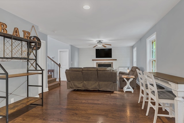 living room with a tiled fireplace, ceiling fan, and dark hardwood / wood-style flooring