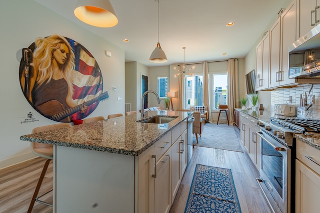 kitchen featuring appliances with stainless steel finishes, sink, light wood-type flooring, hanging light fixtures, and a kitchen island with sink